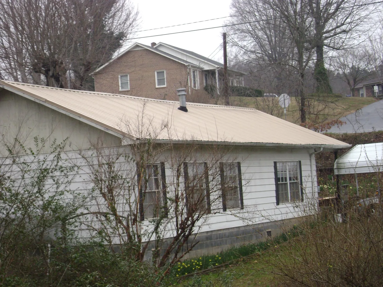 Tan metal roof on a white sided house set into a hillside — Commercial Roofing by Roofing Brothers in Carbondale
